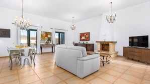 A spacious living room with a sofa, dining table, and chairs, a fireplace, and a television. - Villa Palm View by Villa Plus (Corralejo)