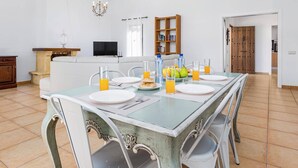 A dining area with a table set for four, chairs, a chandelier, a television, and a bookshelf. - Villa Palm View by Villa Plus (Corralejo)