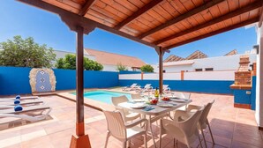 Un espace extérieur abrité comprenant une piscine, des chaises longues et une table à manger pour six personnes.