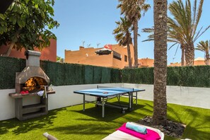 Eine Terrasse mit Steinofen, Tischtennisplatte und einer kleinen Sitzecke mit Handtuch.