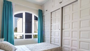 Een slaapkamer met een bed, een raam met gordijnen en een witte kast.