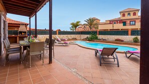 A covered outdoor area with a pool, lounge chairs, and a barbecue grill.