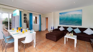 A spacious living area with a dining table, a brown sofa, and a large ocean wave painting on the wall.