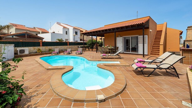 A swimming pool with a curved design, surrounded by lounge chairs and a covered patio area.