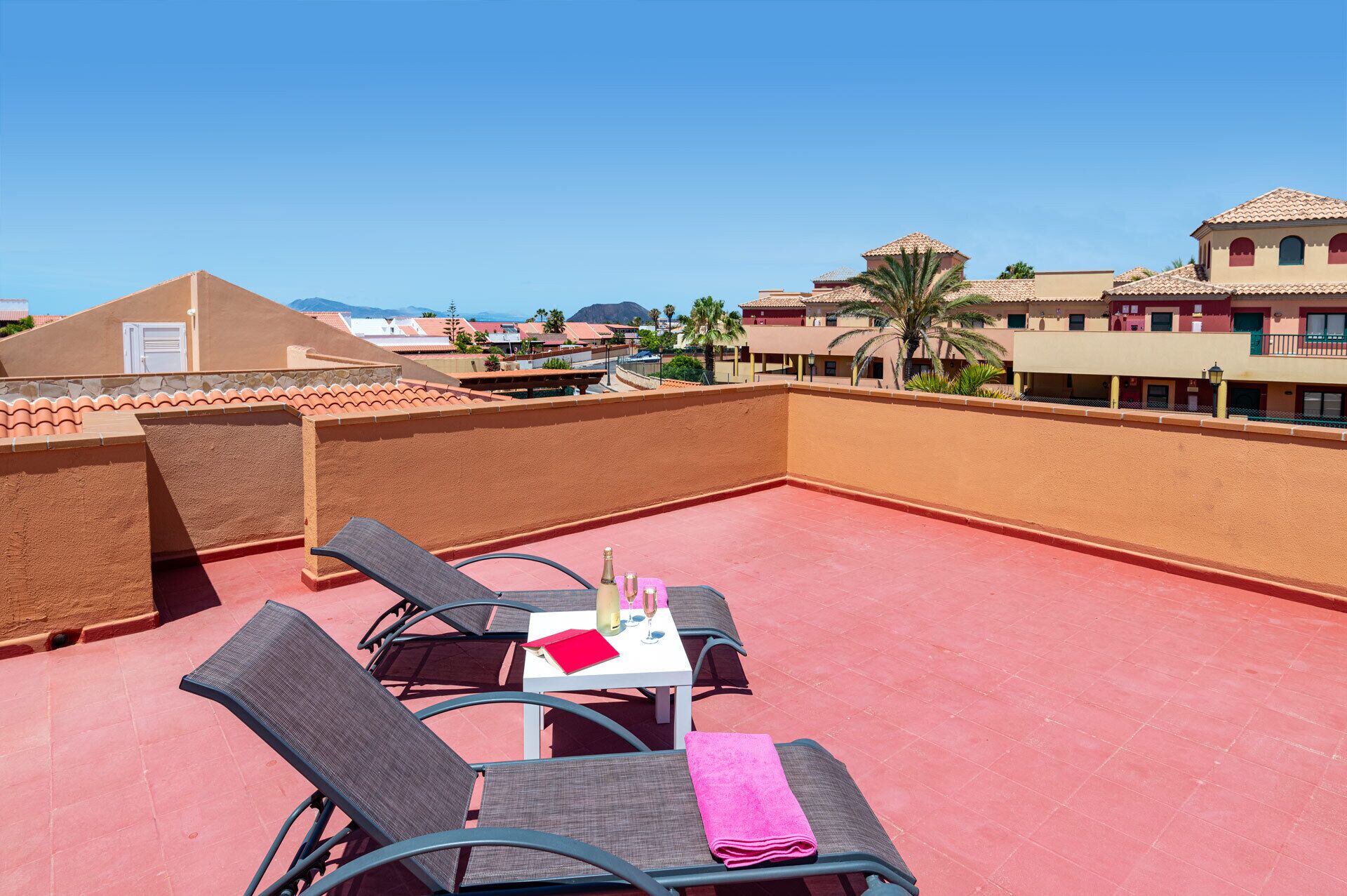 A rooftop terrace with two chairs and a table, a clear view of the surrounding buildings, and a red-tiled roof.