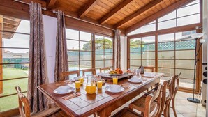 A dining area with a wooden table set for breakfast, large windows, and a view of a backyard. - Villa Sherry by Villa Plus (Corralejo)