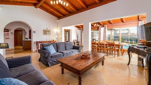 A spacious living area with a wooden ceiling, a sofa, a coffee table, and a dining area with a TV. - Villa Sherry by Villa Plus (Corralejo)