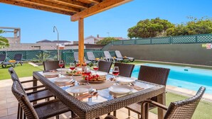 An outdoor dining area with wicker chairs and a table set for a meal, overlooking a swimming pool. - Villa Sherry by Villa Plus (Corralejo)