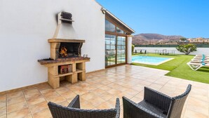 Un patio con una parrilla de piedra, una piscina y sillones de descanso.