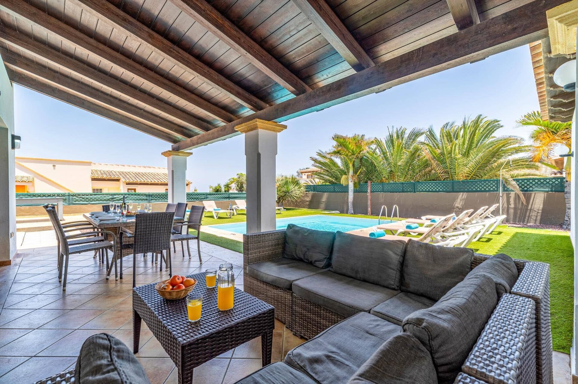 Un espacio al aire libre techado con piscina, sillas de descanso y una zona de estar con mesa y sillas.