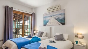 Ein Hotelzimmer mit zwei Betten, einem großen Fenster mit Vorhängen, einem Gemälde von einem Pier und einer Klimaanlage.