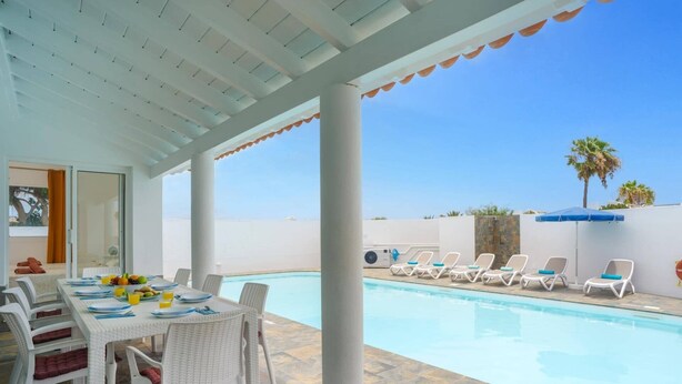 A covered outdoor area with a pool, lounge chairs, and a dining table with chairs. - Villa Esmeralda by Villa Plus (Corralejo)
