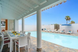 Un espace extérieur abrité comprenant une piscine, des chaises longues et une table à manger avec des chaises.