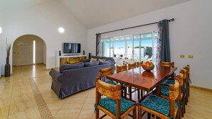 A spacious living area with a sofa, TV, and dining table with chairs. - Villa Esmeralda by Villa Plus (Corralejo)
