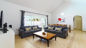 A living room with two grey sofas, a wooden coffee table, and a glass door leading to an outdoor area. - Villa Esmeralda by Villa Plus (Corralejo)