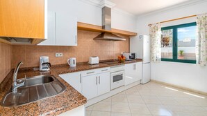 Una cocina moderna con encimeras de granito, muebles blancos, un lavamanos de acero inoxidable, horno integrado y ventana con vistas.