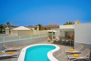 A pool area with lounge chairs and a table, surrounded by a white building with a view of mountains. - Villa Olivina 2 by Villa Plus (Tías)