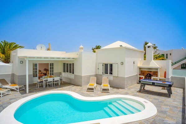 A poolside area with a swimming pool, lounge chairs, a barbecue grill, and a small dining setup. - Villa Olivina 2 by Villa Plus (Tías)