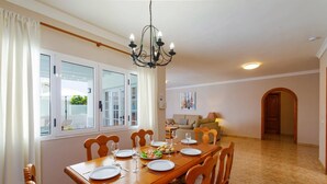Ein Essbereich mit einem Holztisch, gedeckt für vier Personen, einer Kristallleuchtre und Blick durch große Fenster.