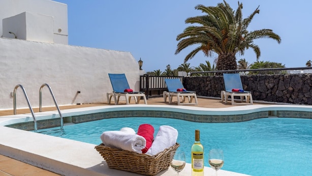 Un área de piscina con sillones reclinables, una cesta de mimbre con toallas y una botella de vino.