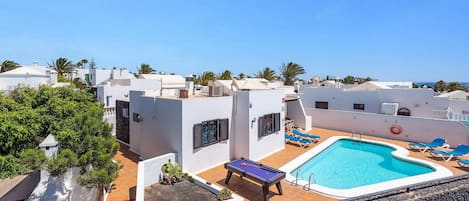 A rooftop pool area with a pool table, lounge chairs, and a clear view of the surrounding buildings and palm trees.