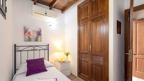 Un dormitorio con cama, una mesita de noche con lámpara, un amplio armario de madera y un equipo de aire acondicionado.