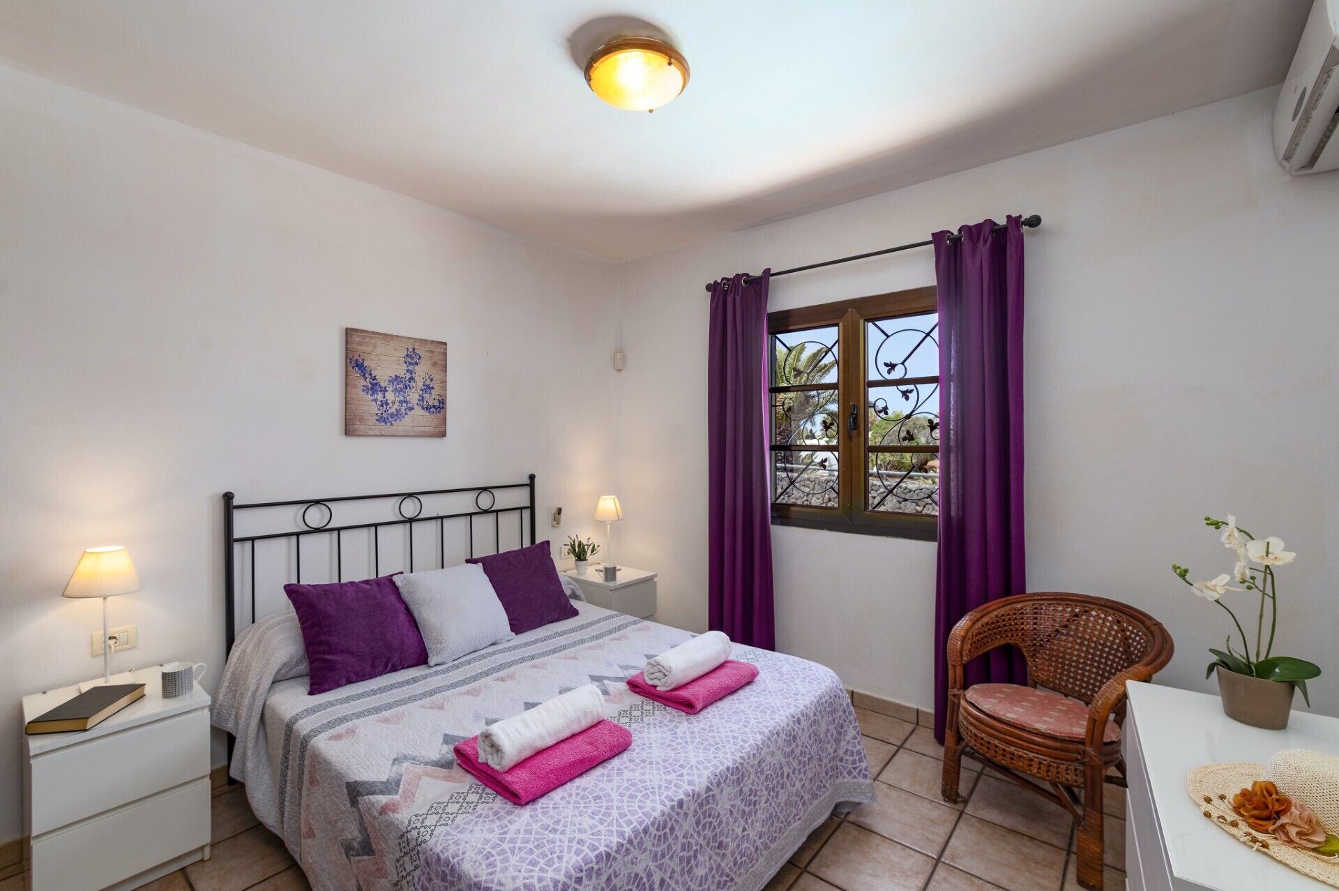 Une chambre à coucher avec un lit, une table de chevet, une chaise, une fenêtre avec des rideaux et une plante en pot.
