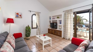 Una sala de estar con sofá, mesa de centro, televisor y balcón con mobiliario exterior.