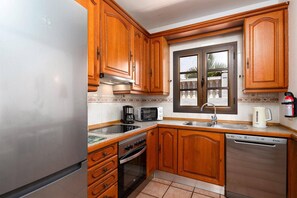 A kitchen with wooden cabinets, a stainless steel refrigerator, a microwave, a coffee maker, a dishwasher, and a window with a view of a balcony.