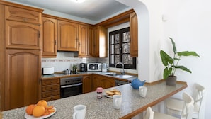 Una cocina con armarios de madera, encimera de granito, horno empotrado, microondas, cafetera y ventana con pared de piedra.