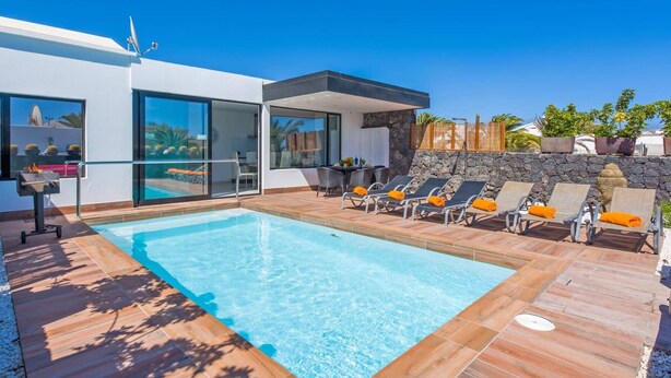 A modern pool area with a clear blue pool, lounge chairs, and a stone wall. - Villa Kikay by Villa Plus (Tías)