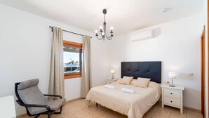 A bedroom with a bed, bedside tables, a chair, a window with curtains, and a chandelier.