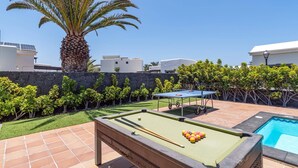 Een biljart tafel met biljartballen, een kleine pooltafel en een palmboom in een achtertuin.