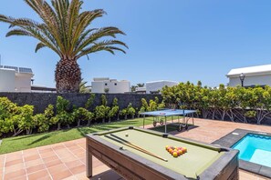 Een biljart tafel met biljartballen, een kleine pooltafel en een palmboom in een achtertuin.