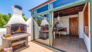 An outdoor patio with a stone barbecue grill, a glass door leading to an interior dining area, and a wooden door.