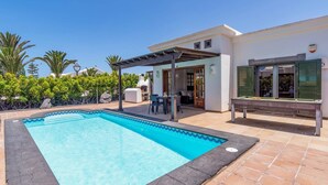 A swimming pool with a covered patio area, a barbecue setup, and a billiards table.