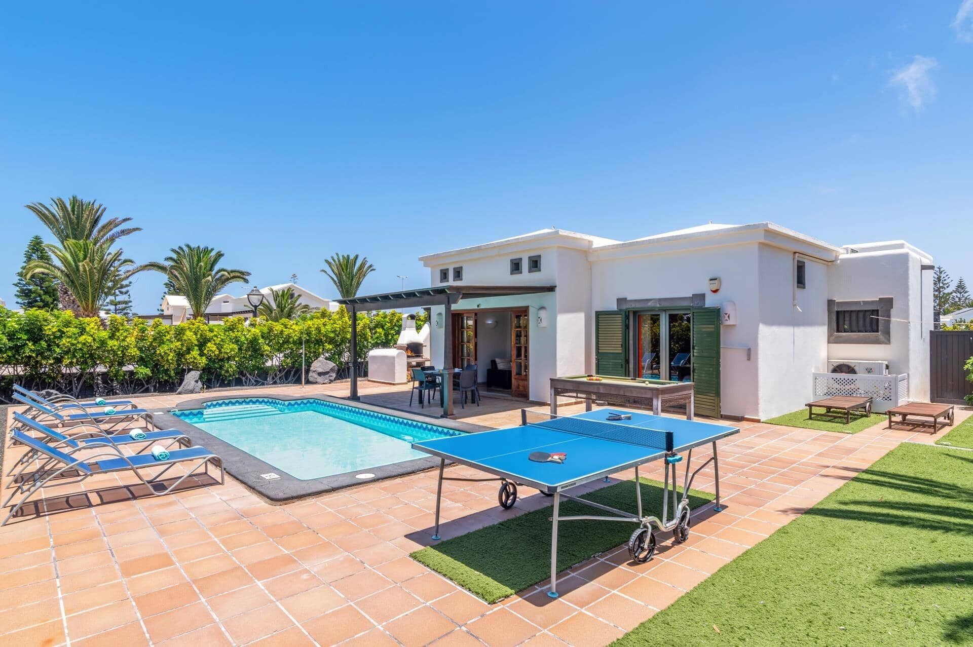 A pool area with lounge chairs, a ping pong table, and a building with a patio.