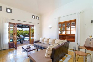 Una sala de estar con un sofá, una mesa de centro y un comedor con una mesa y sillas. Hay una puerta que conduce a un área exterior con piscina.