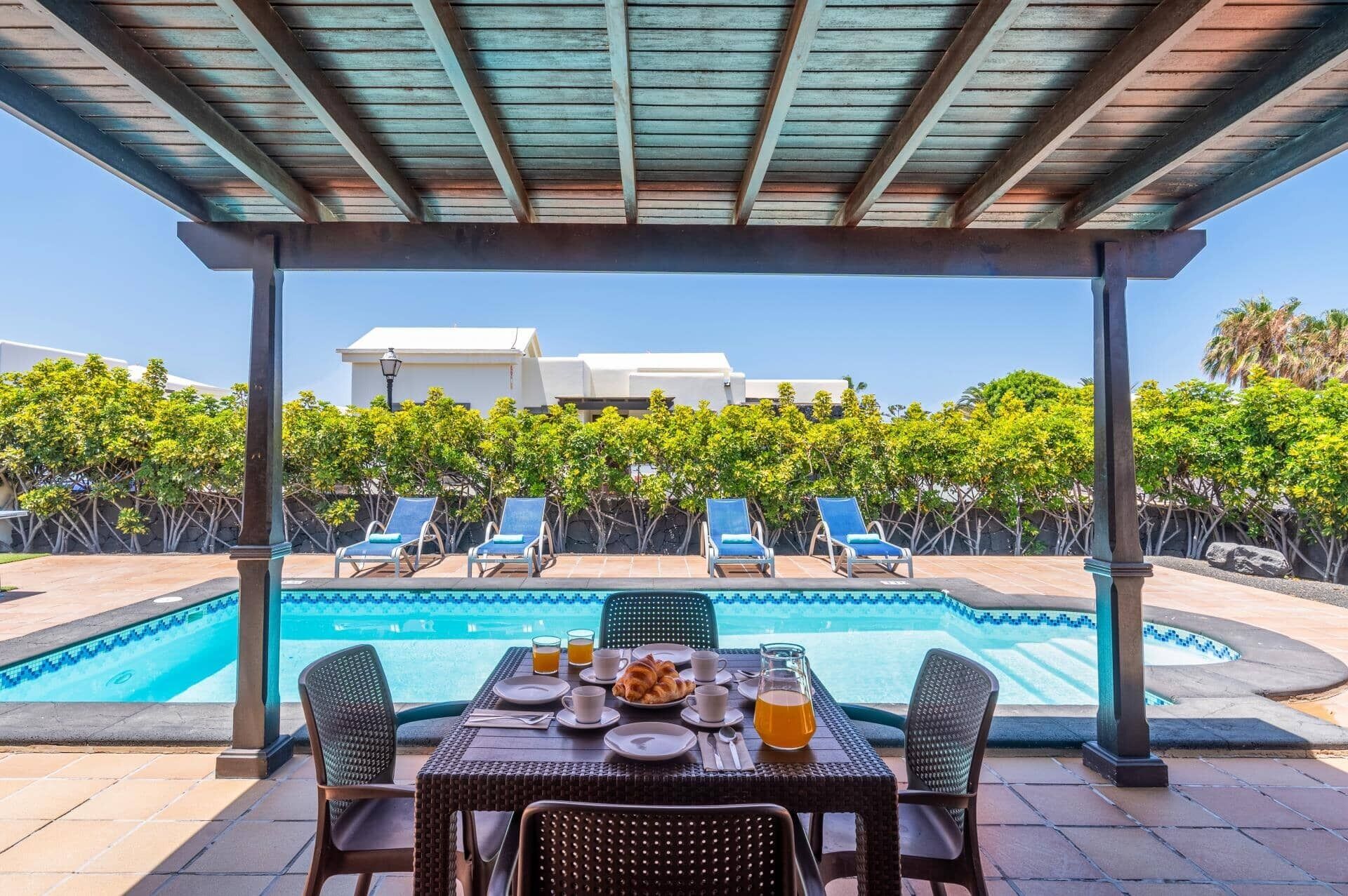 A poolside area with a table set for breakfast, lounge chairs, and a view of a building in the background.