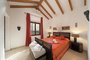 Un dormitorio con una cama, dos mesitas de noche, una ventana con cortinas y un aire acondicionado instalado en la pared.