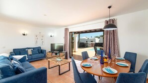A living room with a sofa, TV, coffee table, and dining area with chairs and plates. - Villa Yaiza by Villa Plus (Playa Blanca)