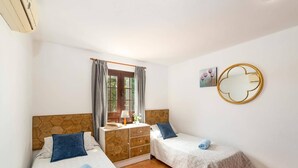 A bedroom with two beds, a wooden dresser, a window with curtains, a round mirror, and a small painting on the wall. - Villa Yaiza by Villa Plus (Playa Blanca)