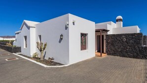 A modern white building with a stone wall, a cactus, and a clear blue sky. - Villa Yaiza by Villa Plus (Playa Blanca)
