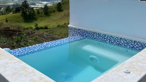 Een vierkant bubbelbad met een betegelde rand, met een bergachtig landschap op de achtergrond.