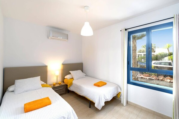 A hotel room with two beds, a nightstand with a lamp, and a window with a view of the outside. - Villa Lomo Blanco by Villa Plus (Playa Blanca)