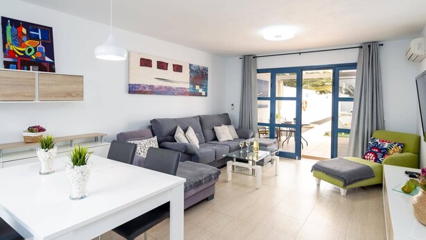 Un salon moderne avec un canapé gris, une table à manger blanche et un fauteuil vert. On y trouve une table basse en verre et un tableau accroché au mur.