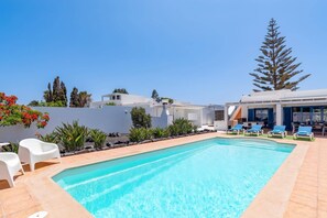Una piscina con lettini, un edificio bianco e un albero alto.