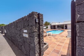 Un mur de pierre orné de panneaux, une piscine et un bâtiment moderne doté d’un patio.