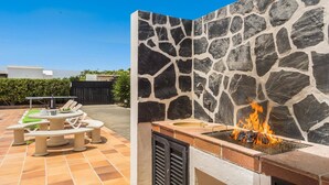 Patio esterno con muro in pietra, barbecue con fiamme vive e posti a sedere all'aperto.