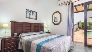 Una camera da letto con una testiera in legno, due comodini con lampade, un letto grande con copripiumino a righe e vista sull'esterno tramite una porta vetrata.